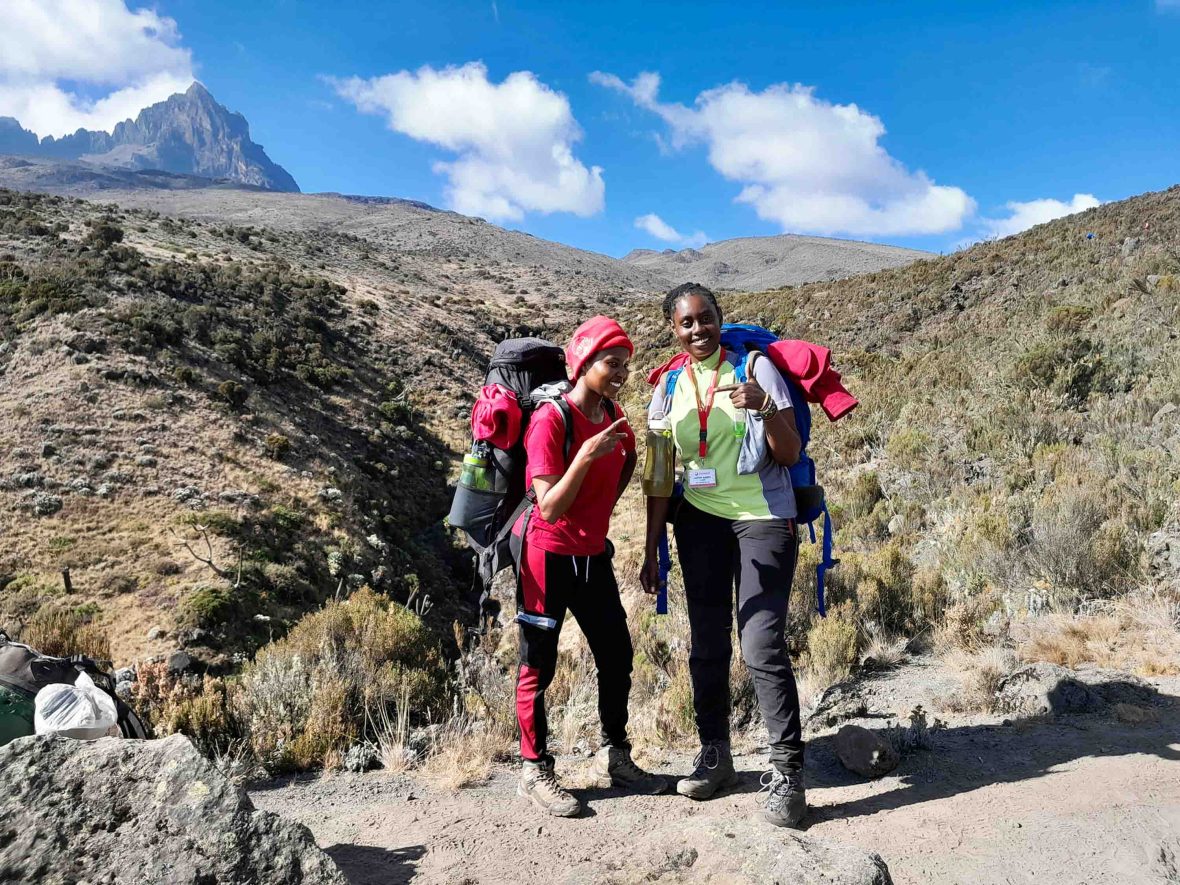 Two women stand on a mountain smiling.